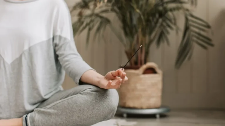 Zdjęcie przedstawia osobę medytującą, z zapalonymi kadzidełkami do medytacji, które pomagają w stworzeniu spokojnej, duchowej przestrzeni.