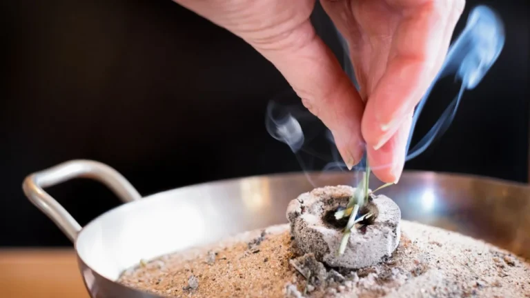 Jak palić kadzidło bez węgielka – ręka umieszczająca kadzidło w metalowym naczyniu z unoszącym się dymem.